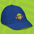 Load image into Gallery viewer, Blue cap with embroidered Mr. Stumble design on a green background